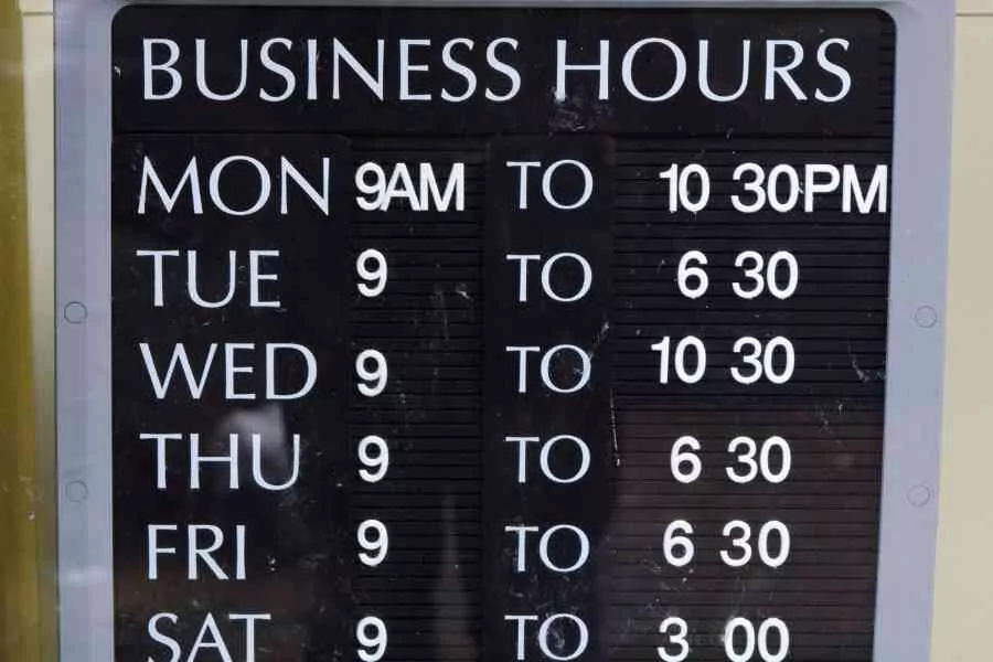 A Business Hours Sign Showing Opening Times For Each Day Of The Week With Varying Closing Hours.