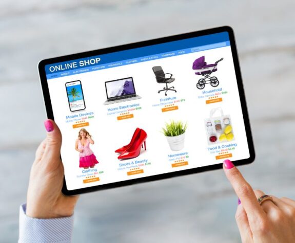 Hands Holding A Tablet Displaying An Online Store Webpage With Various Product Categories Such As Electronics, Home Goods, And Beauty Products.